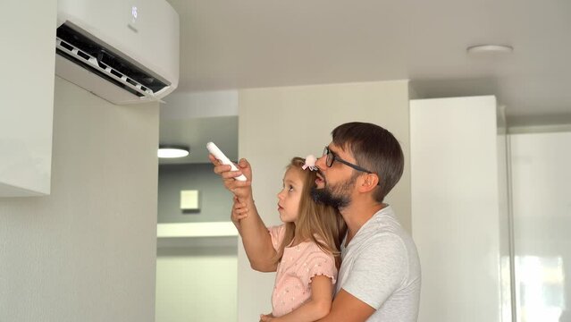 Happy family, father and little girl turn on air conditioner using remote control. Cooler system