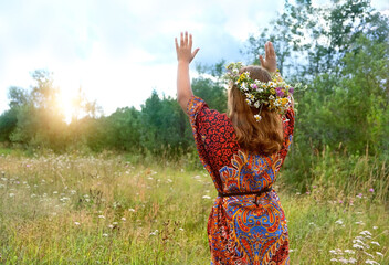 girl in flower wreath on green meadow, abstract natural background. Floral crown, symbol of summer...