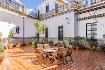 Fototapeta na wymiar Andalusia patio with a wooden table and chairs, wall decorated with beautiful tiles and floor with brown porcelain paving with interspersed tiles