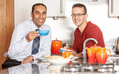 Gay Lifestyle: Good Morning. A same sex couple with bright smiles enjoying breakfast together in their modern home. From a series of related images.