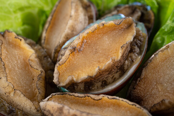 Delicious raw abalone in a plate on wooden table background.