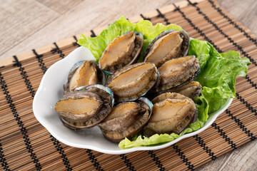 Delicious raw abalone in a plate on wooden table background.