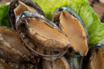 Delicious raw abalone in a plate on wooden table background.
