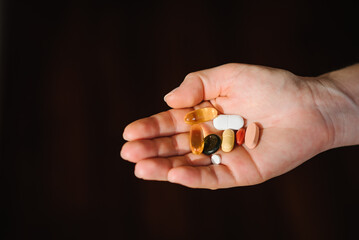 Woman hand with omega 3, multivitamins, vitamins B, C, D, collagen tablets, probiotics, iron capsule. Hand hold supplements on blurred background. Unrecognizable woman takes vitamins daily. Top view.