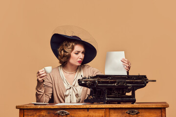 Attractive woman writer wearing old-fashioned clothes sitting at typewriter with surprised face...