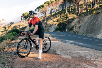 Fototapeta premium Smiling cyclist standing on a roadside in wild terrain. Male bike rider standing with his bicycle at taking a break.