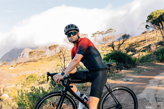Portrait of a professional cyclist in helmet and glasses standing with bicycle against wild terrain.