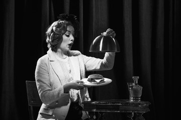 Monochrome portrait of adorable woman wearing vintage costume holding burger with surprised face and open mouth
