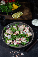 Vegetarian salad of fresh arugula, radish and mushrooms in a plate on a dark background