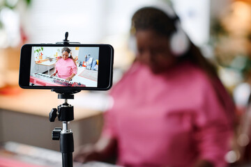 African American woman recording her performance on piano on smartphone sitting in the room