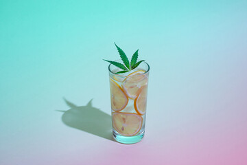 Neon lighted glass of water with ice, lemon slices and marijuana leaf against gradient color background. Minimal metaverse summer concept.