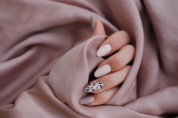 A woman's hand with a beautiful manicure is holding a silk fabric. Autumn trend, beige color...