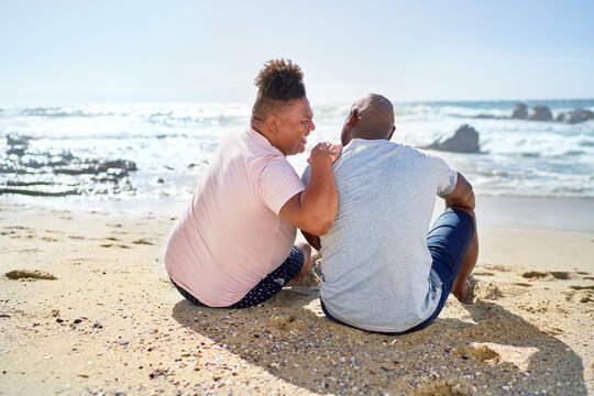 Gay male couple laughing on sunny ocean beach
