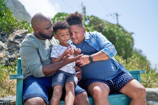 Gay male couple and son sitting on sunny beach bench
