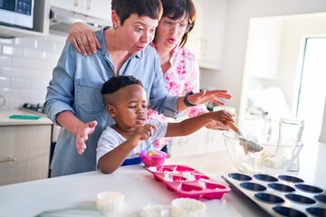 Lesbian couple and cute son baking heart-shape cupcakes in kitchen