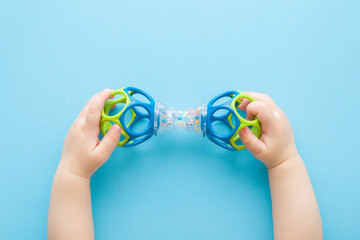 Baby boy hands playing with colorful rattle dumbbell on light blue table background. Pastel color....