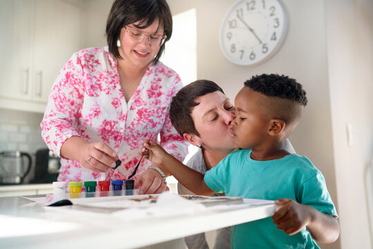 Affectionate lesbian couple kissing son painting in coloring book