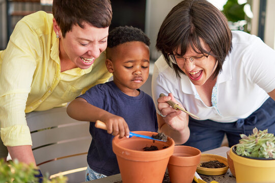 Happy lesbian couple watching son planting plants in flowerpots