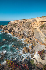 Breathtaking cliffs with crashing waves in the afternoon sun on the Atlantic coast near Vila Nova de Milfontes, Odemira, Portugal. In the footsteps of Rota Vicentina. Fisherman trail. Clear blue sky