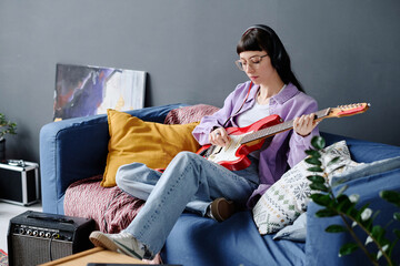 Young woman sitting on sofa in the living room and learning to play guitar