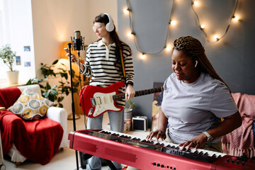 Young women recording song in studio, they singing songs and playing musical instruments during...