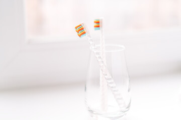 Children's toothbrushes in a glass cup on the windowsill.