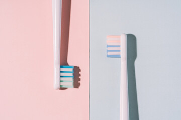 Toothbrushes opposite each other on a blue and pink background.