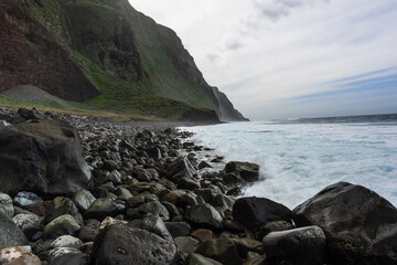 Rocky beach on Madeira Island, green volcanic cliffs at moody weather