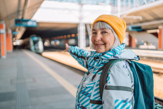 Back view of an adult woman with a backpack in hiking clothes showing the direction of travel while standing at a train station. High quality photo