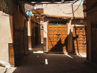 Rays of light in the dusty streets and alleys of the Medina of Marrakech, Morocco, dark city with sunlight, shadow and orange doors