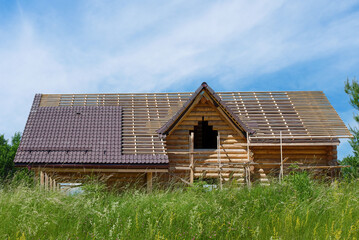 Fototapeta na wymiar New wooden house under construction. Roof tile installation. Tiling roof, construction of cottage. Rural landscape