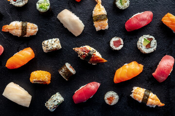 Sushi assortment, overhead flat lay shot. Rolls, maki, nigiri on a black slate background, Japanese food. Salmon, eel, shrimp, tuna etc with rice