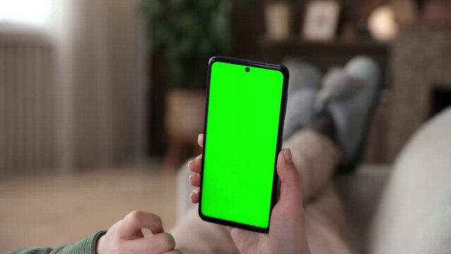 Point of View of woman lying on couch using smartphone with chroma key green screen, doing various gestures like swiping and scrolling - internet, communications concept close up