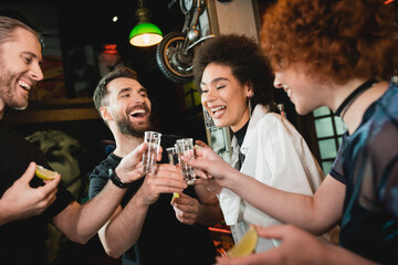 Positive man clinking tequila with interracial friends while spending time in bar.