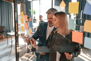 Conception of plan. Many stickers are on the glass. Group of business people are working in the...