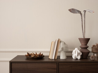 Interior design of aesthetic living room interior with copy space, wooden sideboard, vase with dried flowers, books, modern sculpture, beige wall with stucco and personal accessories. Home decor. 