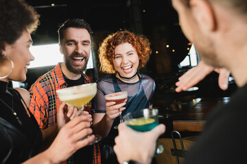 Cheerful multiethnic friends with cold cocktails talking while meeting in bar.