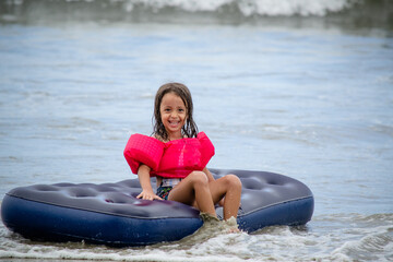 Criança brincando na praia com boia flutuante nas ondas do mar na cor azul e rosa.