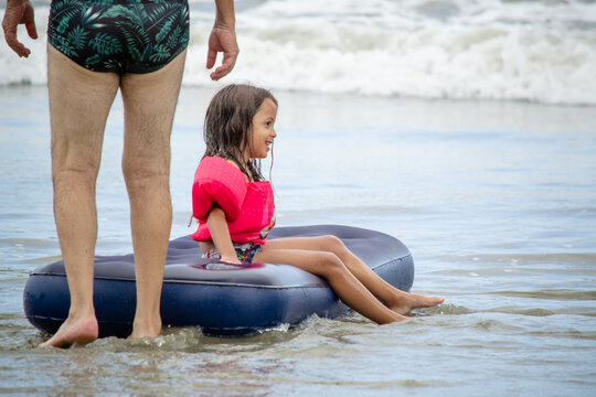 Crian&ccedil;a brincando na praia com boia flutuante nas ondas do mar na cor azul e rosa.