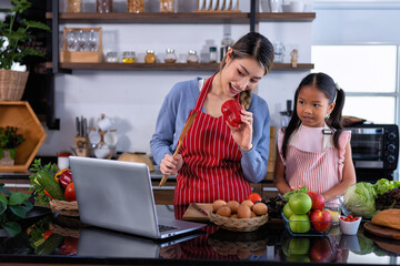 Young mother teach daughter in the kitchen learn online cooking clean food from the laptop computer