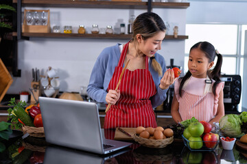 Young mother teach daughter in the kitchen learn online cooking clean food from the laptop computer
