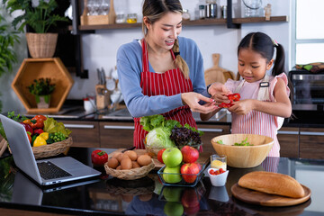 Young mother teach daughter in the kitchen learn online cooking clean food from the laptop computer