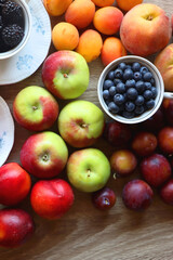 Berries in vintage porcelain dishes, other healthy fruit and vegetable on wooden table. Top view.