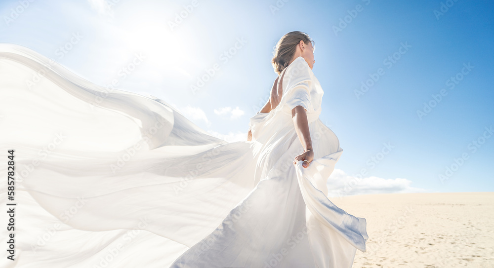 Wall mural photo of a woman in amazing white wedding dress posing on the desert, sunny light, blue sky,