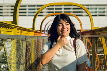 portrait of pensive young latina woman standing on a pedestrian bridge in college.