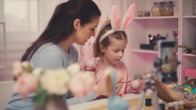 Little girl and mother decorating Easter eggs, recording video tutorial for blog
