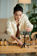 Serious woman setting camera on smartphone and filming video on handmade soap for social media
