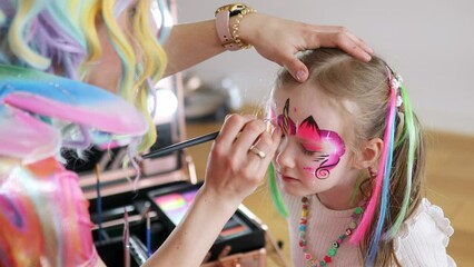 Children face painting. Artist painting little preschooler girl like unicorn on a birthday party. Creative activities for kids