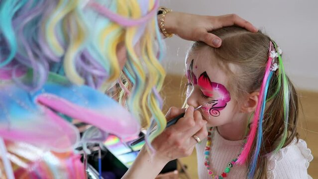 Children face painting. Artist painting little preschooler girl like unicorn on a birthday party. Creative activities for kids