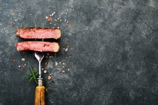 Steaks T-bone. Slices of beef grilled meat barbecue steak on meat fork on burned dark wooden background with copy space for your text. Top view. Mock up.